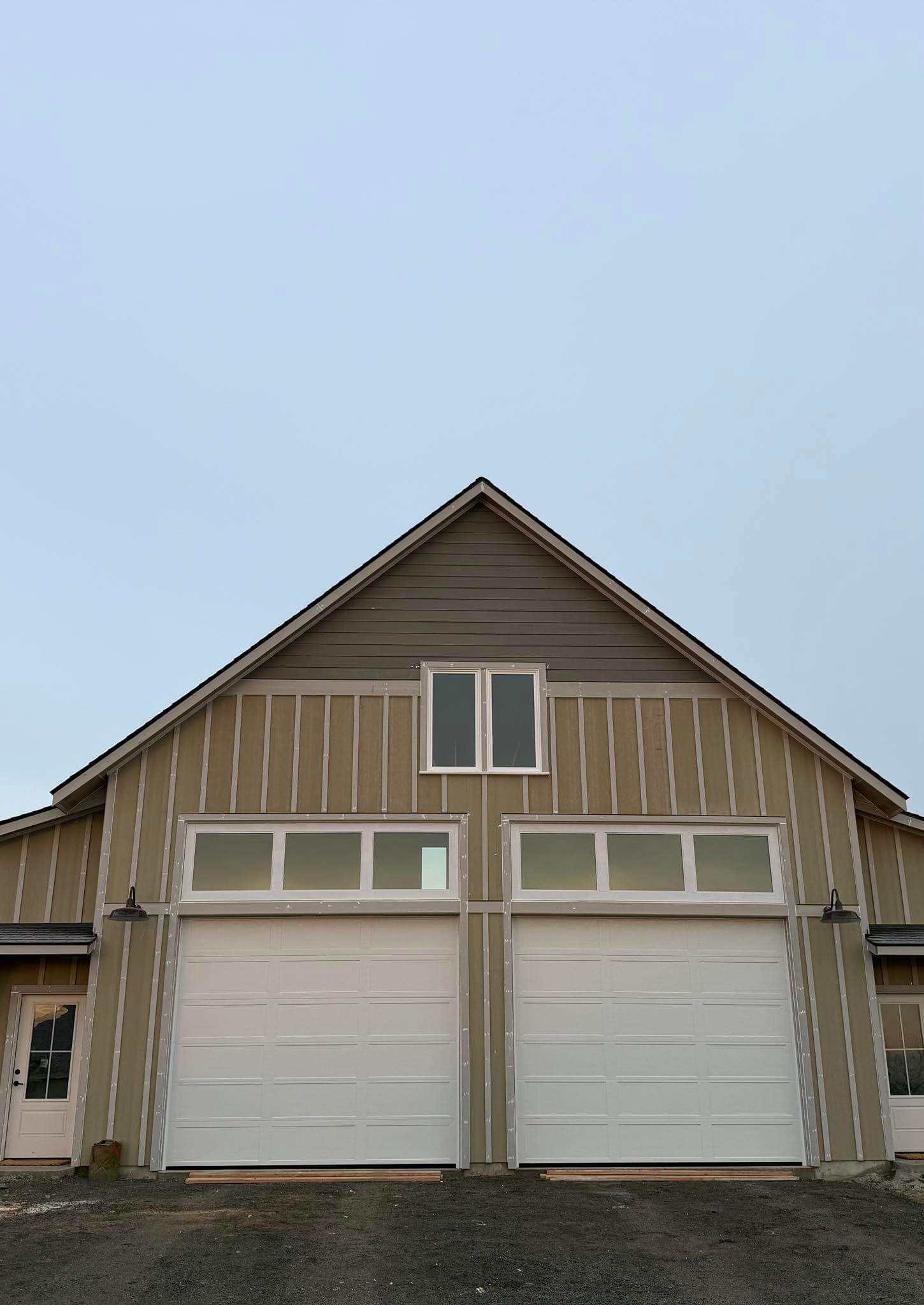 New construction building with two white garage doors and vertical siding, featuring a simple, modern design under a clear daytime sky.