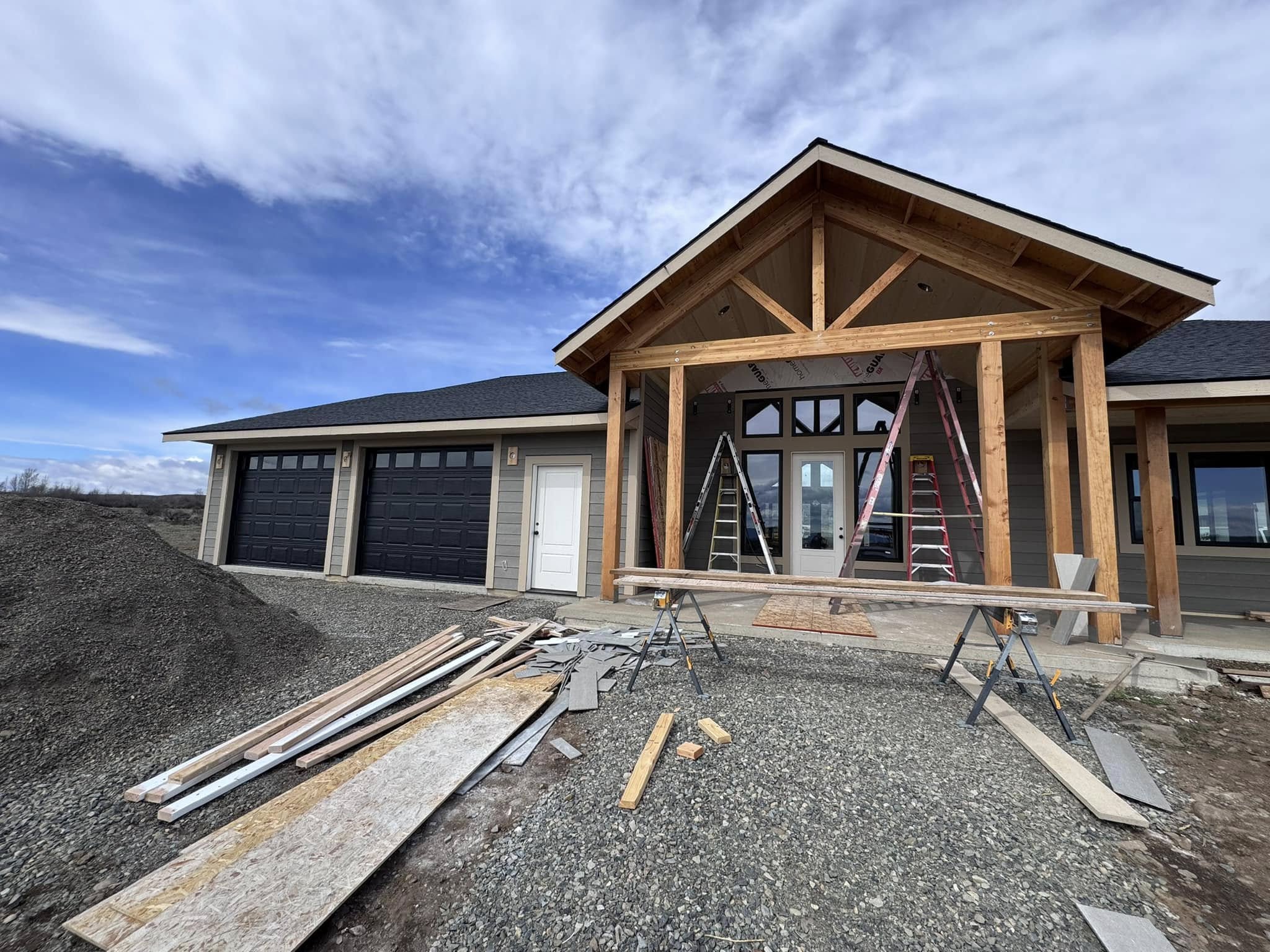 outside view of new house construction with 2 black garage doors and timber framing
