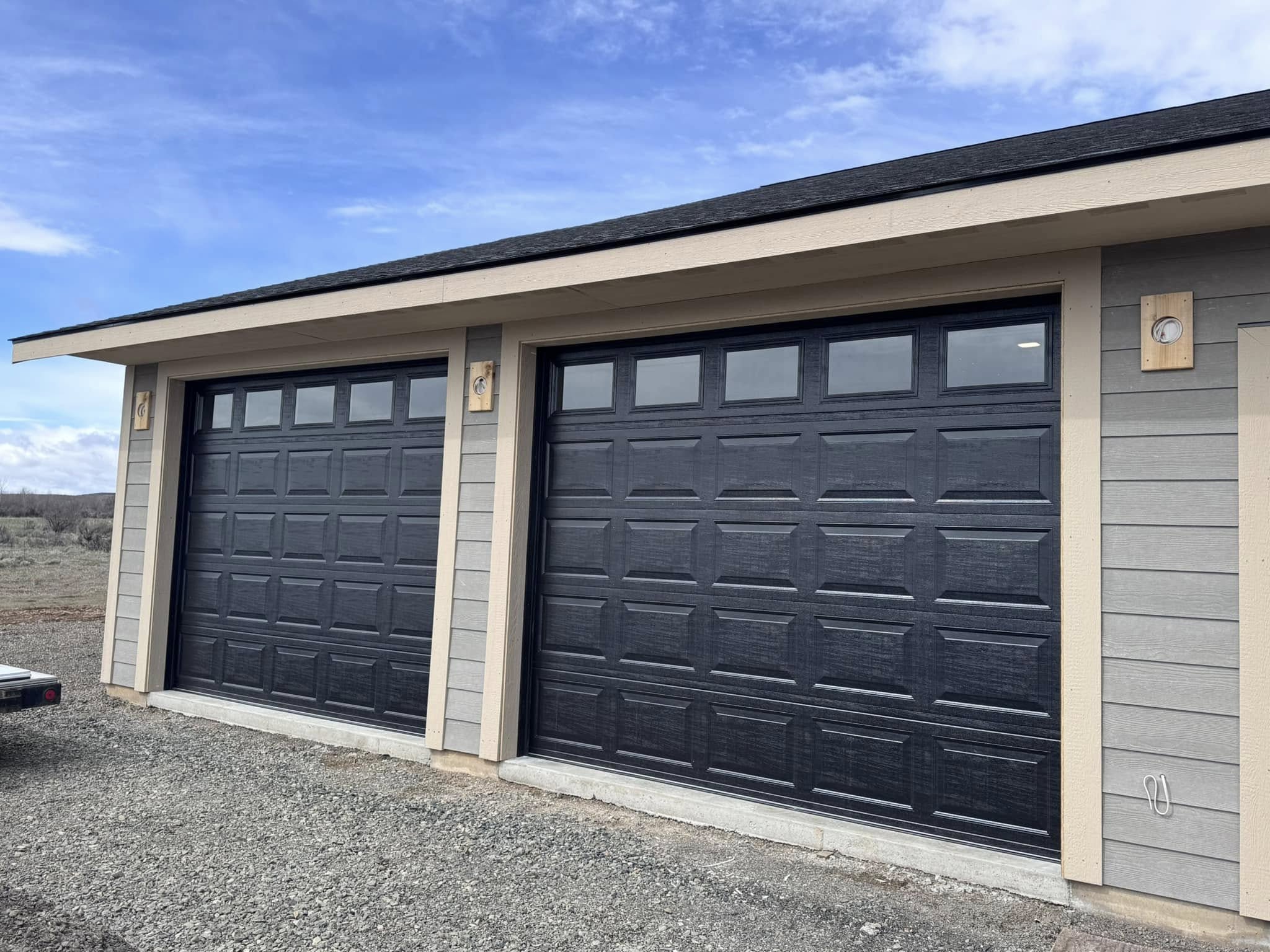 two black garage doors on a grey house with windows